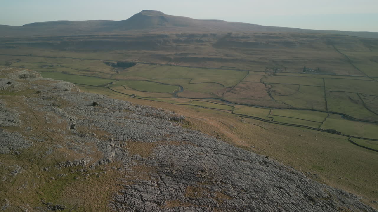 volando sobre la ladera rocosa con la montaña en la distancia y el valle verde debajo en ingleton, yorkshire, reino unido