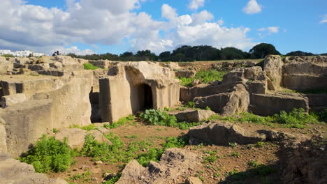 Multiple-entrances-to-burial-chambers-at-the-Tombs-of-the-Kings,-set-against-a-rugged-landscape-under-a-clear-sky