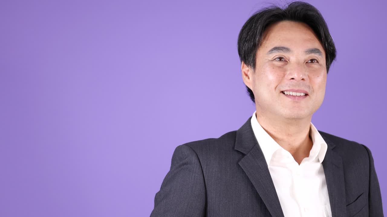 Asian man in business suit smiles confidently, well-lit studio, static camera, purple backdrop