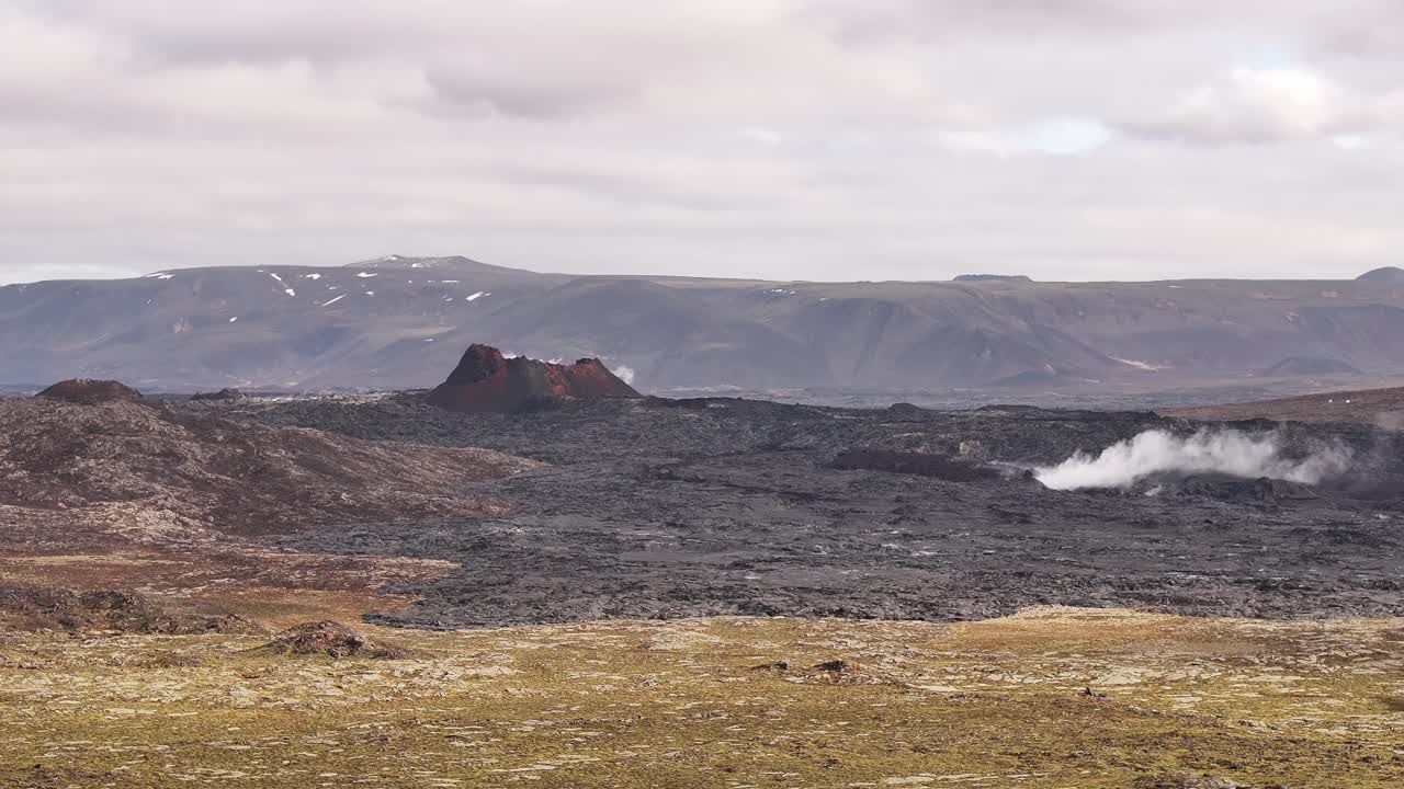 active volcanic cone emits steam across dark lava plain in iceland