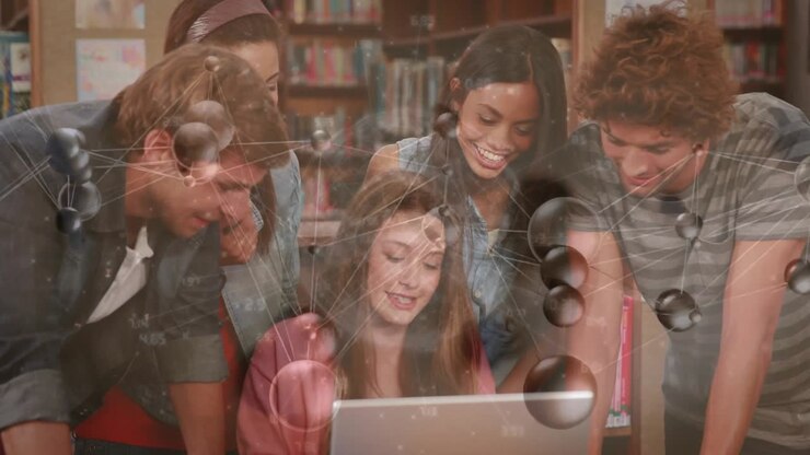 Student scrolling laptop in library activating network graphics while peers leaning in for study
