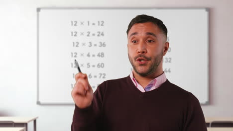 close up shot of mature male teacher in classroom standing in front of board teaching elementary maths lesson