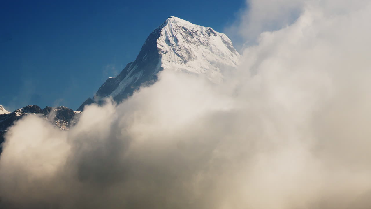 Majestic close-up timelapse of Annapurna South mountain, towering over drifting clouds at sunrise in the Himalayas.