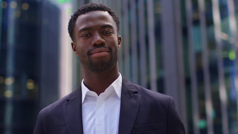 Portrait-Of-Confident-Young-Businessman-Wearing-Suit-Standing-Outside-Modern-Offices-In-The-Financial-District-Of-The-City-Of-London-UK