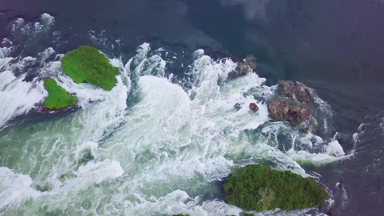 Top down aerial view of the source of the Nile river featuring white water rapids, cascades, green vegetation, and rocks, located in Jinja, Uganda, Africa, drone ascending shot