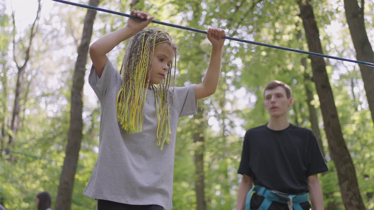 Active child fearlessly climbs the ropes between the trees. Girl in an adventure park are pass obstacles on the rope road. children camp summer camp