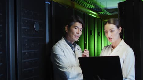 Diverse-female-and-male-it-technicians-in-lab-coats-using-tablet-and-laptop-checking-computer-server