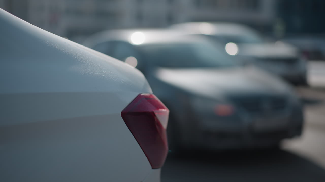 Closeup side car light in foreground with cars moving along city street in winter, blurred crosswalk lines and sun glare bokeh, urban commute flow, soft focus traffic background and cold daylight