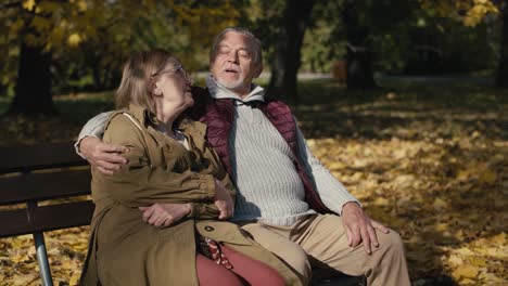 caucasian senior couple sitting at the bench at park and embracing