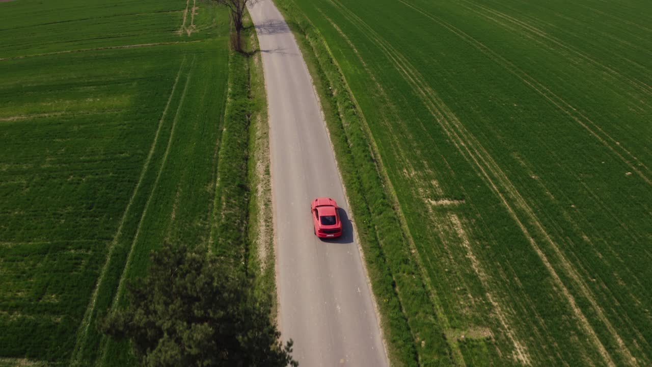 ripresa cinematografica con drone di una ford mustang gt arancione che percorre una strada diritta circondata da campi verdi