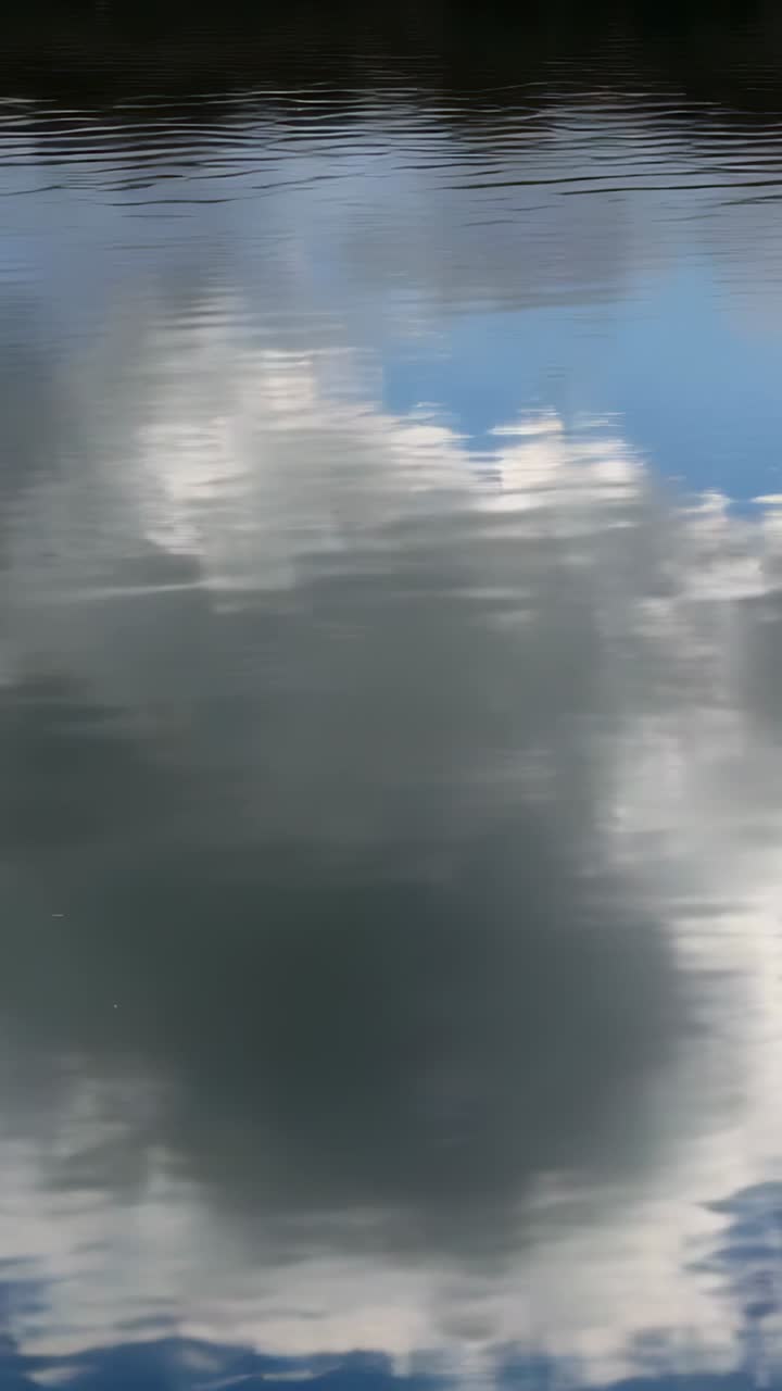 Vertical video: Shifting cloud reflections with dark center patch on lake, breeze making ripples