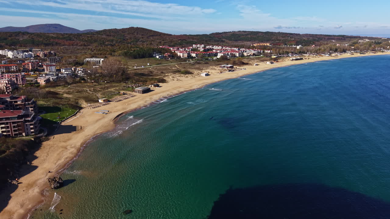 Coastal beauty unfolds under a clear sky with gentle waves lapping the sandy shore, showcasing nature's tranquil charm