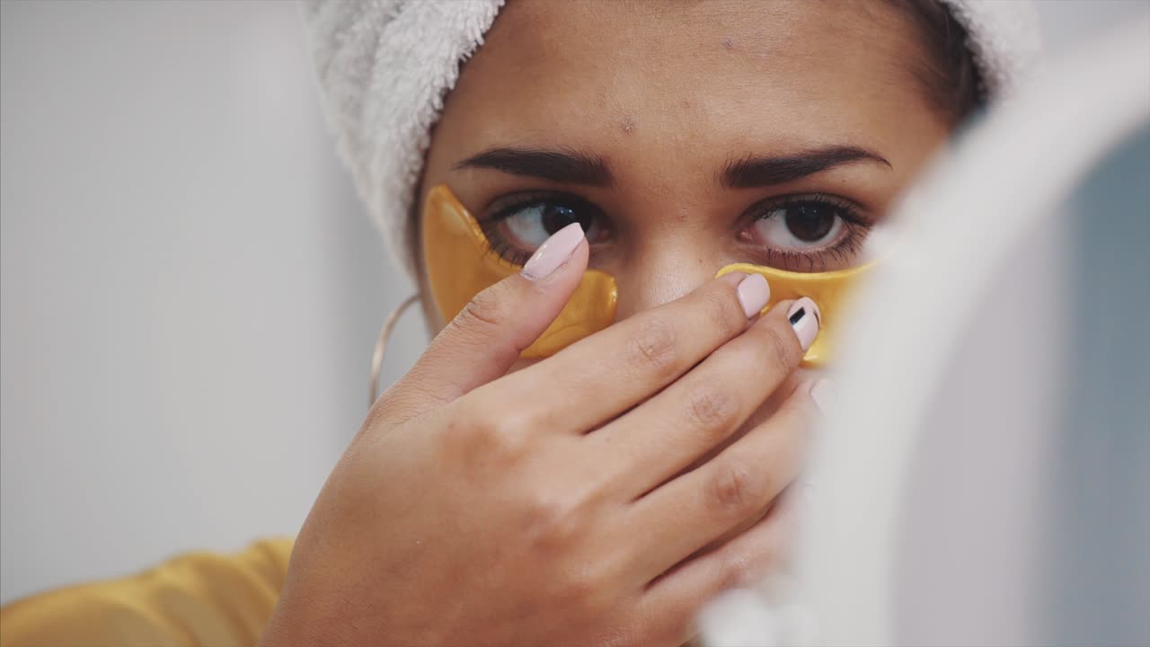A closeup portrait of a beautiful woman after a bath with a towel on the head puts patches under the eyes from wrinkles and dark circles.