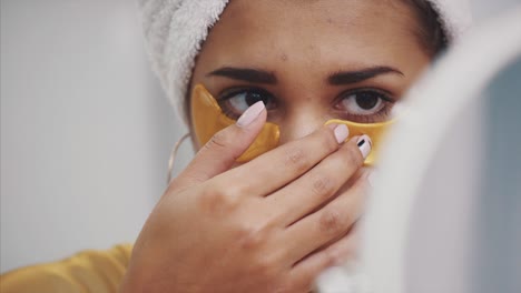 un retrato en primer plano de una mujer hermosa después de un baño con una toalla en la cabeza pone parches debajo de los ojos de arrugas y círculos oscuros.