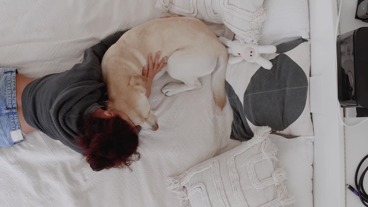 Top-down shot of a woman cuddling and playing with her cute Labrador Retriever at home. Owner and dog share a loving bond, playing together, enjoying quality time in a cozy, pet-friendly environment