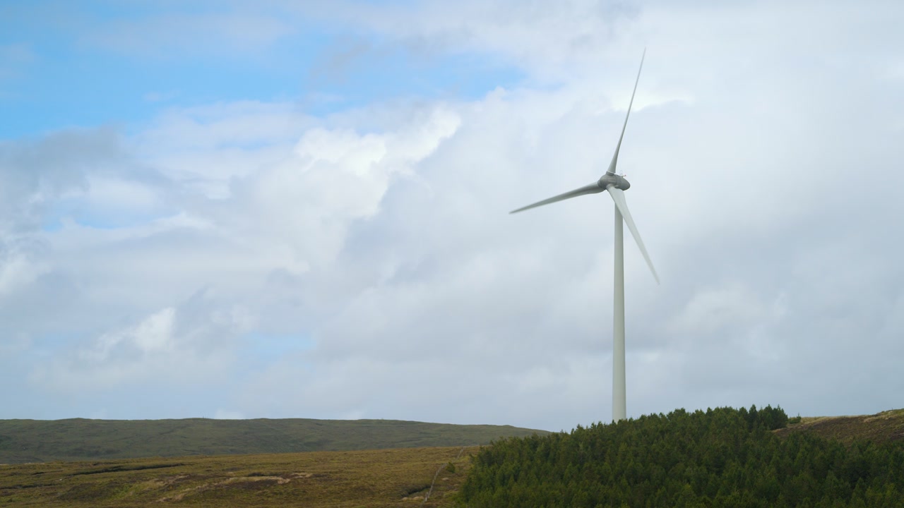Static shot of a solitary wind turbine spinning on a sunny day.