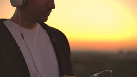 A-man-in-big-white-headphones-listens-to-music-standing-on-the-roof-at-sunset.-Relaxation.