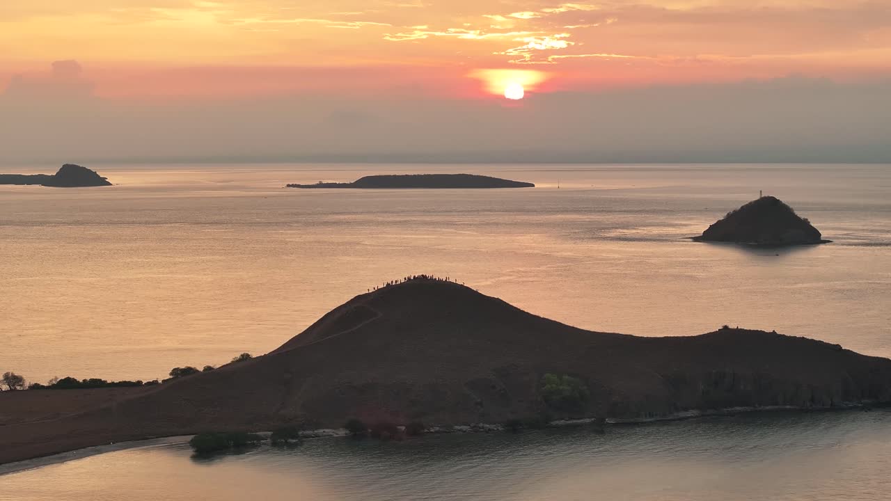 People on hill Gili Kenawa Island watching tranquil sunset on horizon, travel Indonesia.