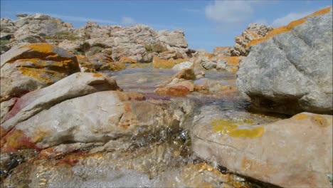 closeup-of-water-running-through-boulders,-rising-to-wide-landscape