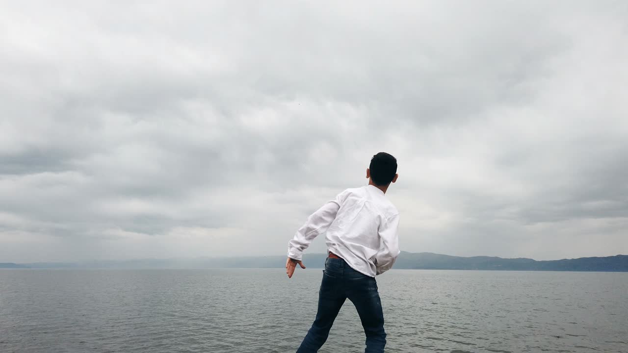 Children stand on the shore of the pond and throw stones, slow motion