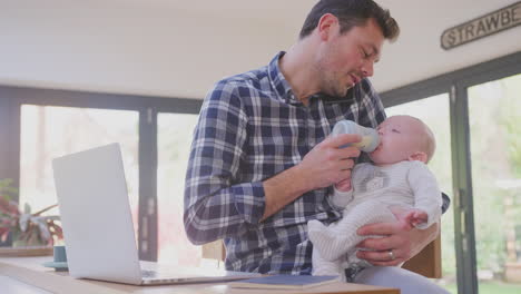 Working-father-multi-tasking-talking-on-mobile-phone-whilst-feeding-crying-baby-son-with-bottle---shot-in-slow-motion