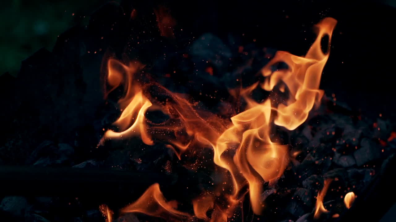 Wooden stick breaks smoldered logs in fire. Bright sparks moving on dark background from glowing fire. Slow motion.