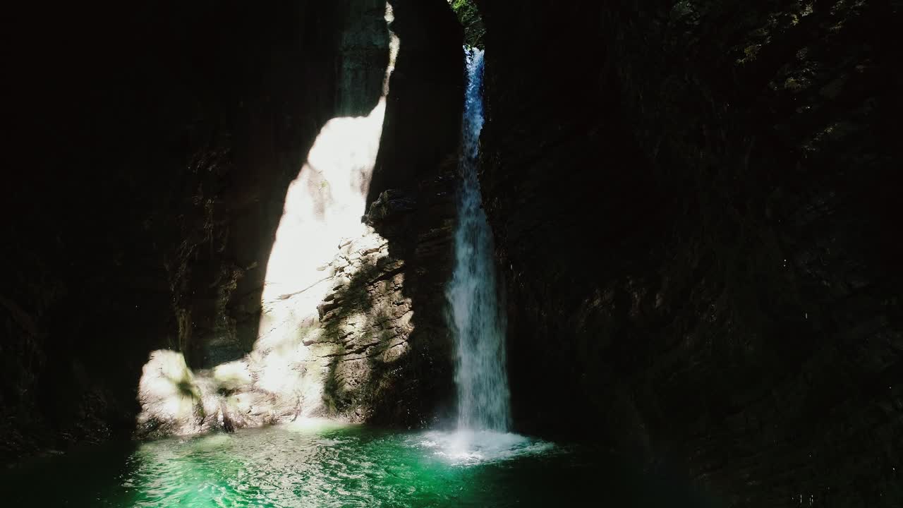 Magical waterfall in cave gorge in Slovenia falls into emerald green water pool