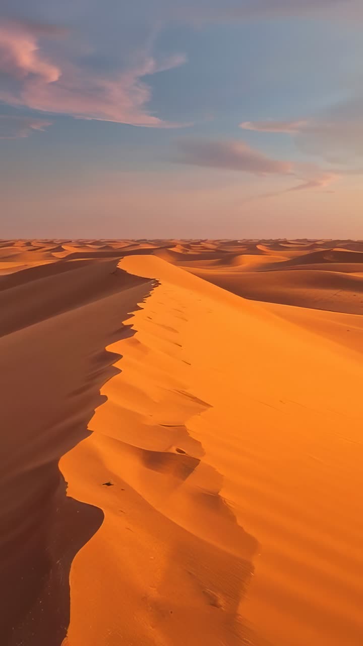 Video verticale: telecamera in movimento che segue la cresta di una duna di sabbia attraverso le dune, mostrando increspature e nuvole rosa