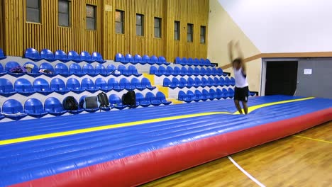 una toma en movimiento de un chico haciendo una secuencia de gimnasia que incluye una vuelta, un salto hacia atrás y una voltereta hacia atrás y hacia adelante en el suelo