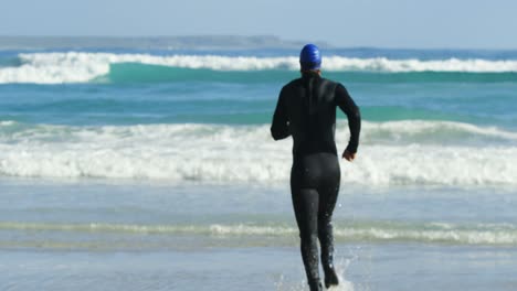 vista trasera del surfista masculino corriendo en la playa