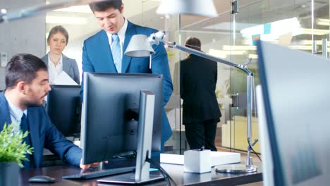 en la oficina grande el asociado trae noticias importantes a su gerente, muestra la tableta con información. el edificio moderno de vidrio y hormigón está lleno de gente de negocios ocupada.
