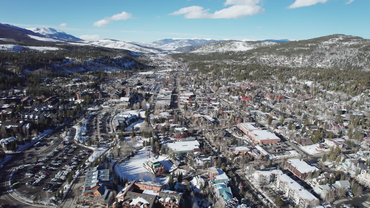 A wide aerial over peaceful and beautiful snow-covered Breckenridge, as cars carrying skis and snowboards drive into the popular Colorado mountain town for a ski vacation at the world famous resort.