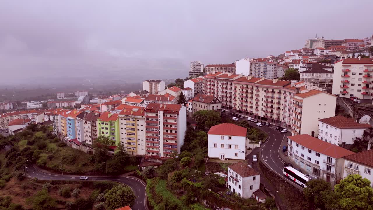 Imagens dramáticas de drone de um conjunto habitacional em Portugal, apresentando um arranha-céus, um bloco de apartamentos e veículos em uma estrada estreita com nuvens ao fundo.