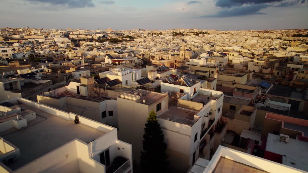 Aerial panning shot over sunlit rooftops of Maltese city during golden hour
