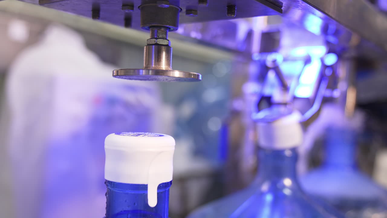 Automatic machine putting and stamping the cork at the flask. Bottles are filled with water at backdrop in blur.