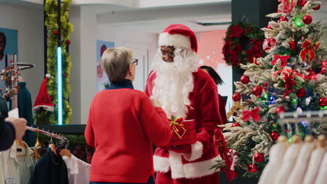 Kunden-Im-Weihnachtsgeschäft-Schmücken-Ein-Bekleidungsgeschäft-Und-Geben-Einem-Arbeiter,-Der-Als-Weihnachtsmann-Verkleidet-Ist-Und-Ein-Geschenk-Hält,-Das-Als-Sammelbox-Dient,-Ein-Tombola-Ticket.-Mitarbeiter,-Der-Eine-Werbeveranstaltung-Für-Die-Winterferien-Organisiert