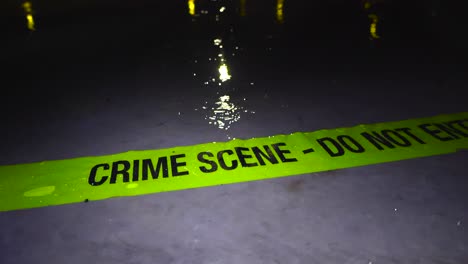 yellow colorful and vibrant crime scene do not enter tape thrown on a concrete slab where raindrops are falling in slow motion at night time. well lit scene and light refelections on the water in back