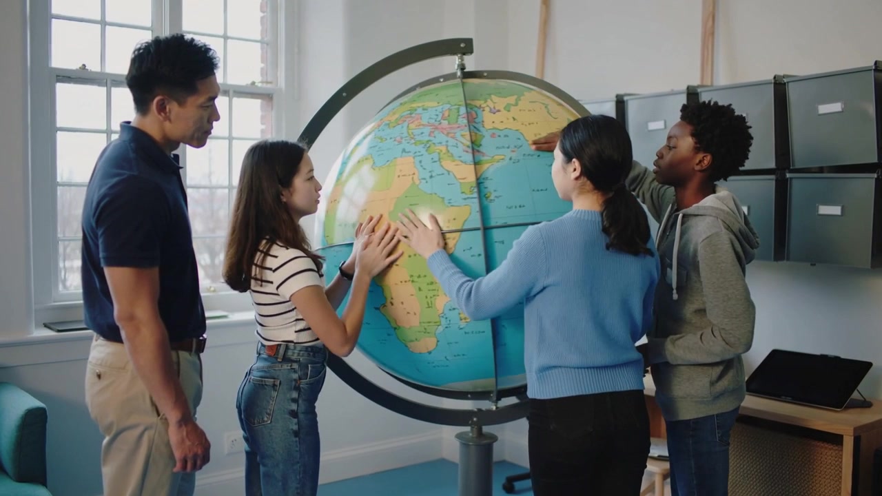 Con le mani, gli studenti ruotano un mappamondo da terra in classe, tracciando le regioni per una lezione di geografia.