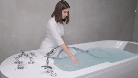a young spa cosmetologist girl adjusts the hydrobath before the procedure. hydromassage bath in the salon. correct water temperature.