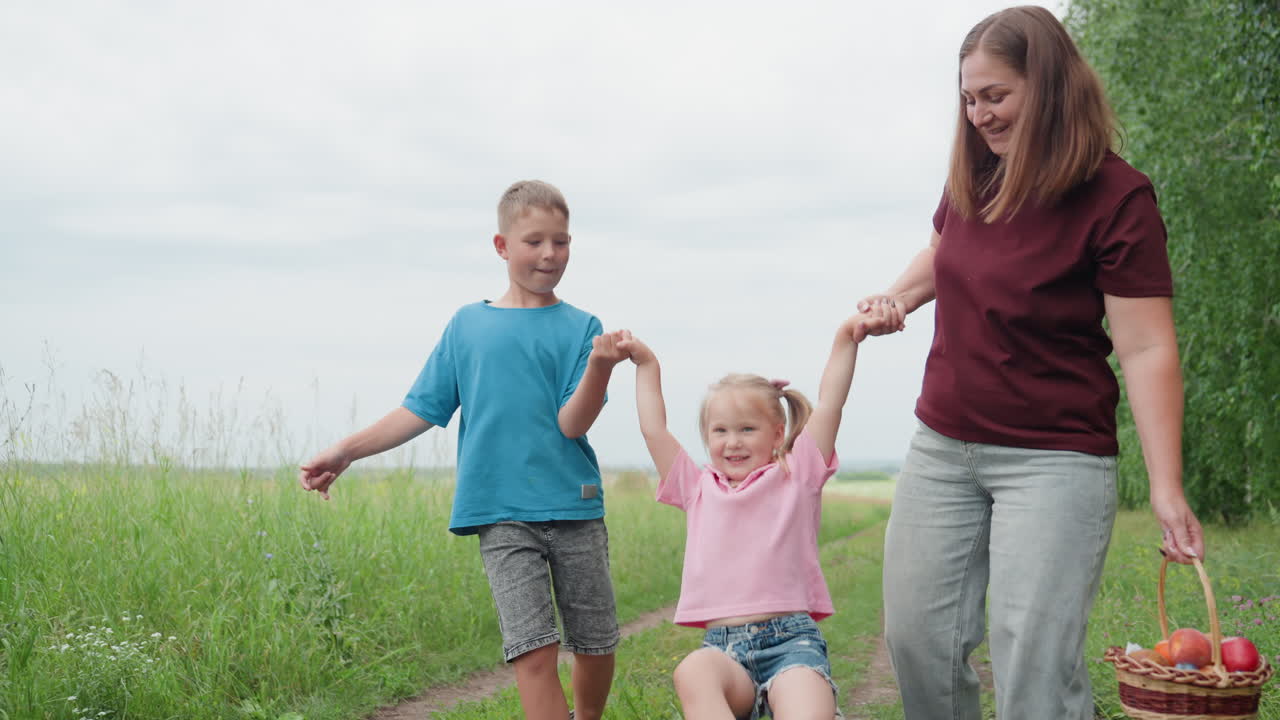 미소를 지으며 사과 바구니를 들고 가는 엄마와 잔디가 깔린 시골길을 걷는 남매와 여동생, 부드러운 흐린 하늘 아래 따뜻한 유대감을 느끼며 장난기 넘치는 흰색 가족
