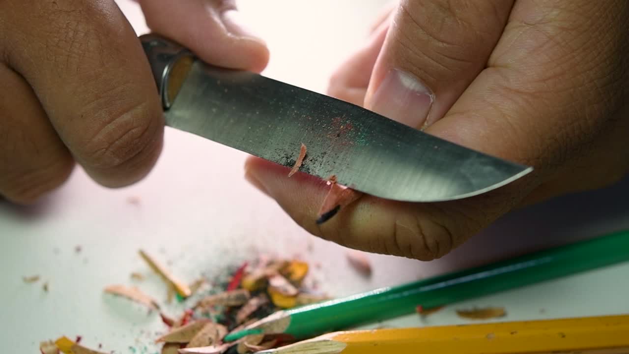 Opptak av hender som sakte spisser en blyant og noen fargeblyanter med en skarp kniv