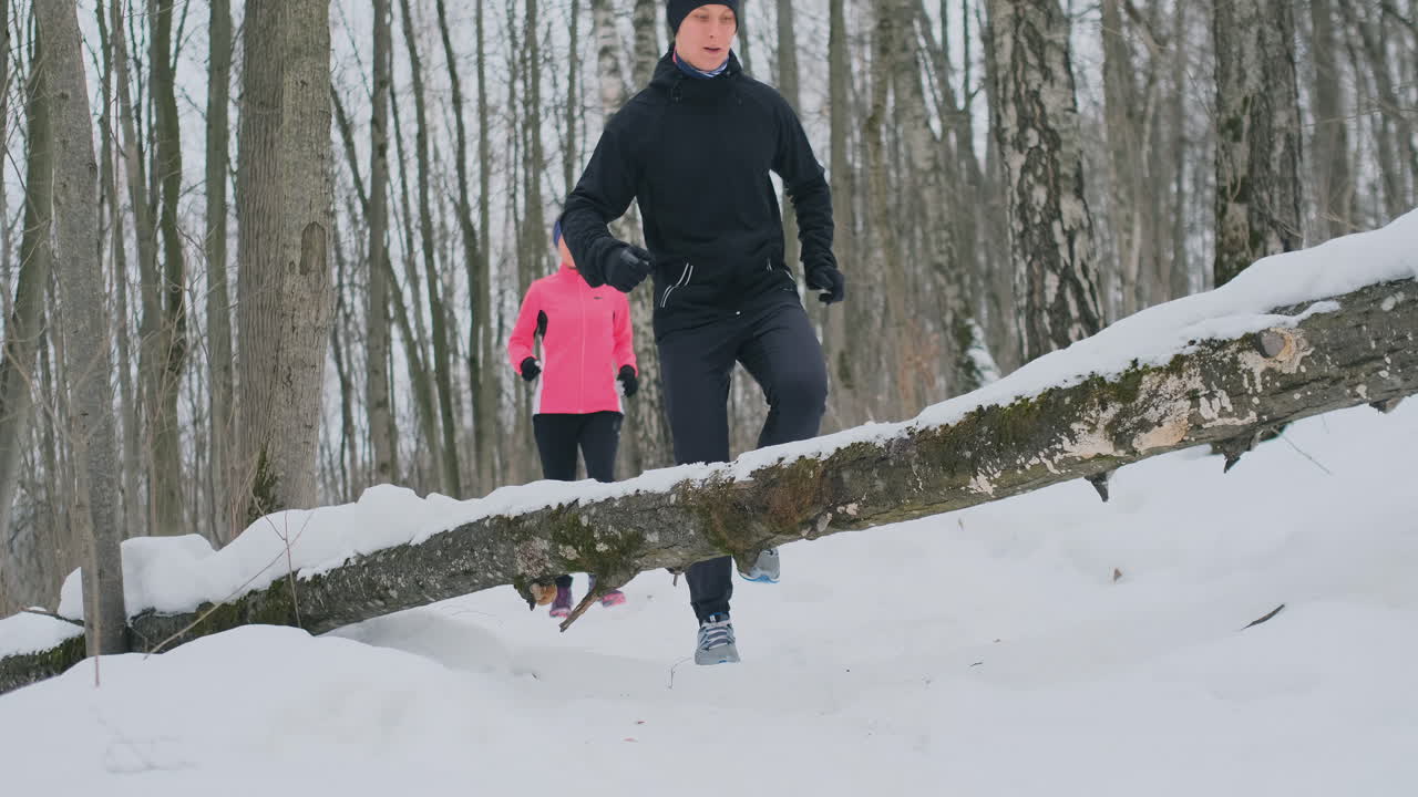 한 남자와 한 여자가 겨울 공원을 달리다가 쓰러진 나무를 뛰어넘는다. 장애물을 넘어