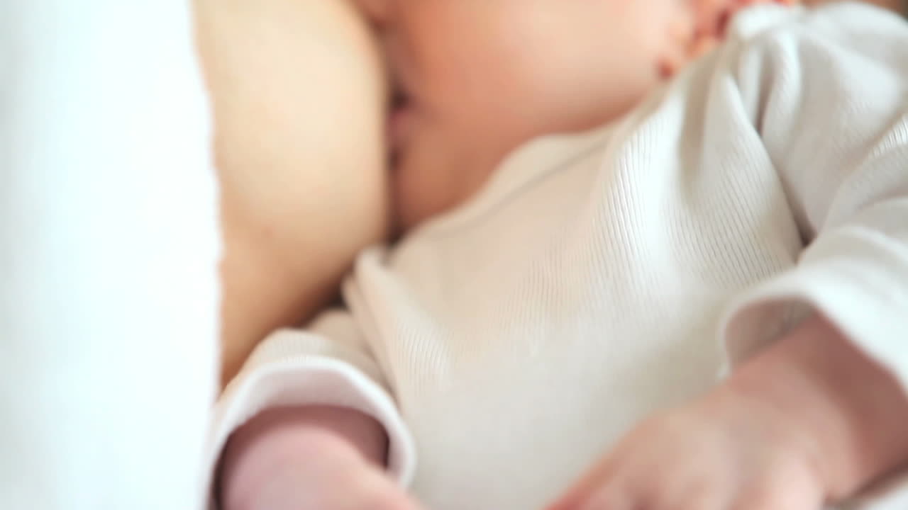 Woman holding babys hands while she breastfeeds