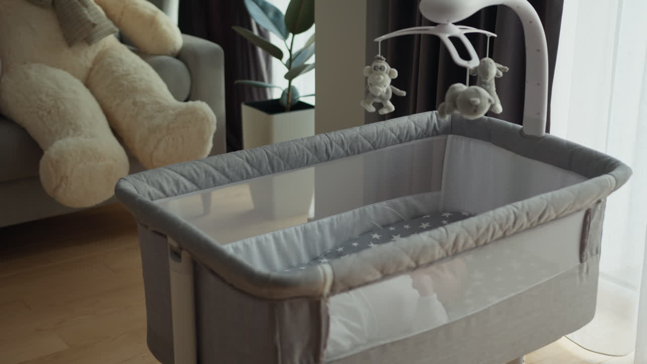 Neonato che dorme nella culla con giostrina, palloncini pastello, orsetto di peluche e giocattoli morbidi sopra