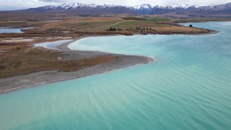 lake tekapo's blue waters and peninsula with southern alps in background. canterbury, new zealand. wide drone shot