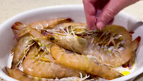 hand sprinkles salt over fresh prawns in bowl