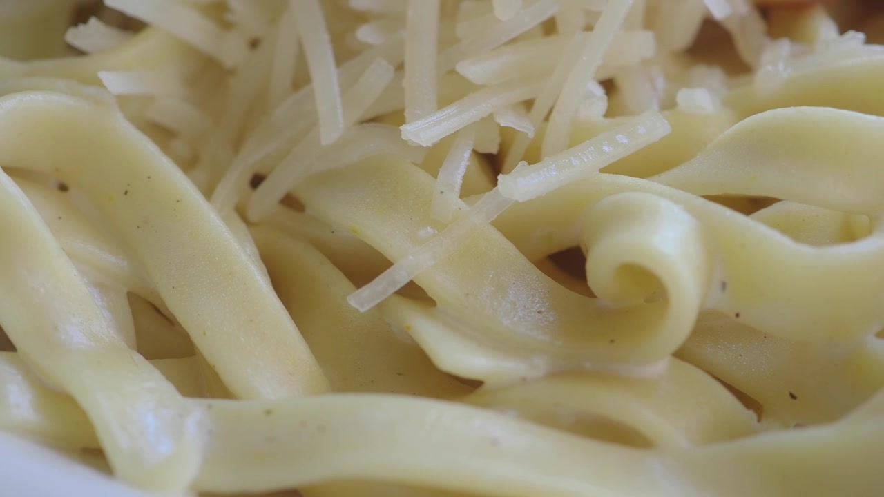 Primo piano di fettuccine cremose con Parmigiano grattugiato.