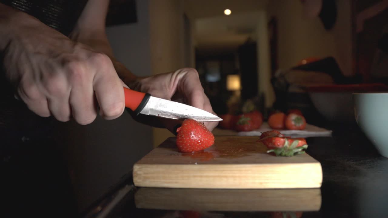 Person Cut The Strawberry Into Half Using Sharp Kitchen Knife On A Chopping Board. - Wide Shot