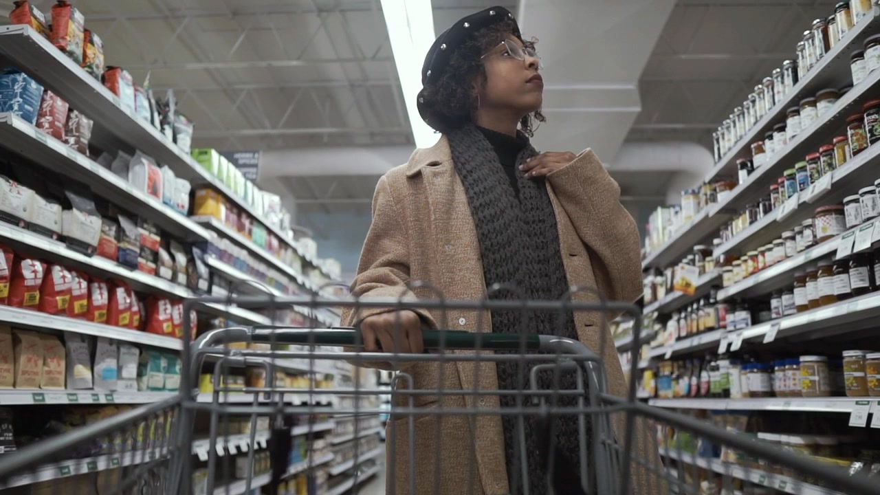 In de supermarkt: mooie Afro-Amerikaanse vrouw duwt een winkelwagen door de versafdeling van een supermarkt