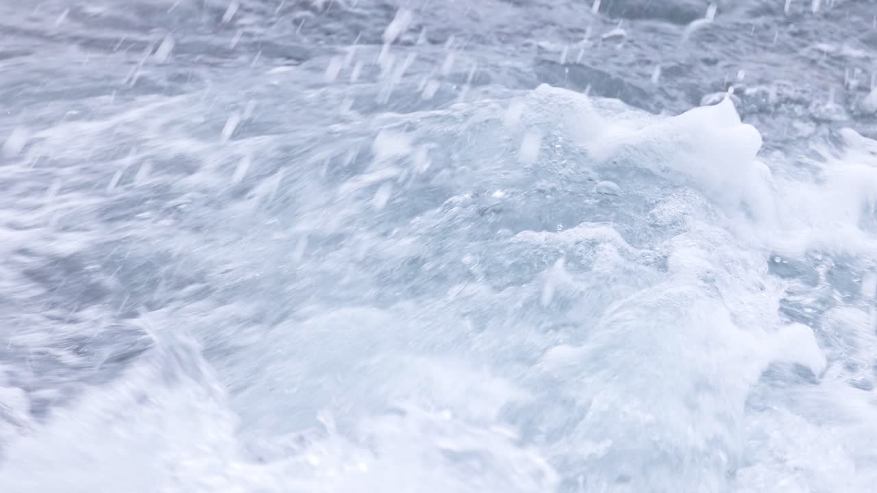 Dynamic ocean waves crash against seaweed-covered rocks, captured with natural lighting and fluid camera movement